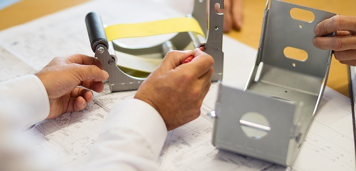 Techniker prüft ein Gehäusebauteil eines textilen Brandschutzsystems anhand einer Konstruktionszeichnung