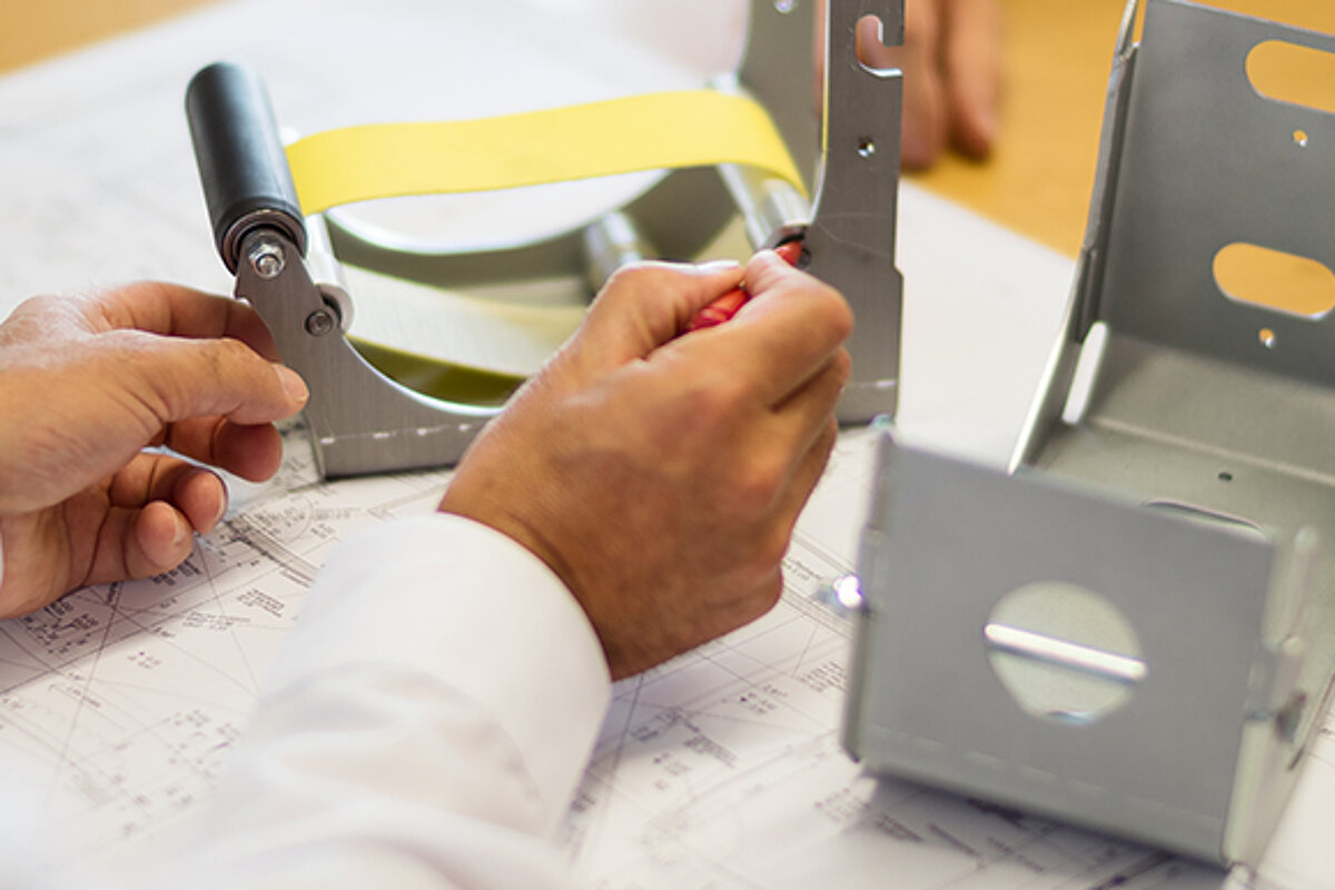 Techniker prüft ein Gehäusebauteil eines textilen Brandschutzsystems anhand einer Konstruktionszeichnung